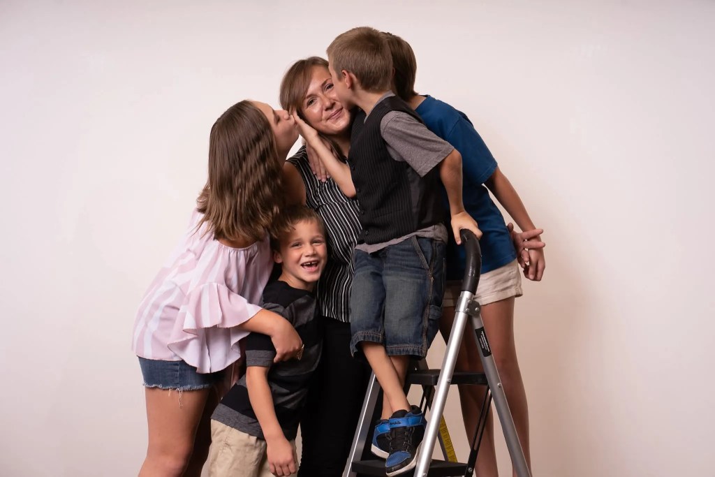 Amber Paton poses for a photo with her four kids surrounding her and kissing her
